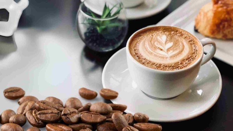Latte art tinh tế cùng hạt cà phê thơm trên bàn trắng
