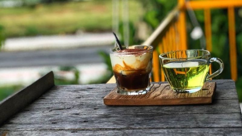 Một ly cà phê đá và trà xanh trên bàn gỗ ngoài trời