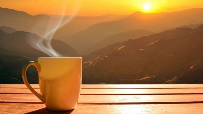 Ly cà phê nóng bốc khói trước khung cảnh núi non hoàng hôn