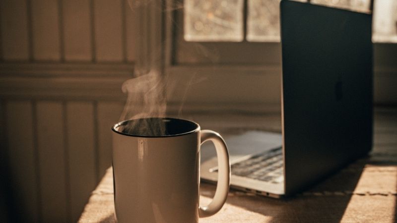 Tách cà phê đen bốc khói bên laptop làm việc hiện đại
