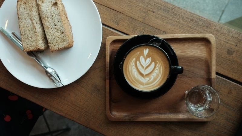 Latte art đẹp mắt cùng bánh mì trên khay gỗ