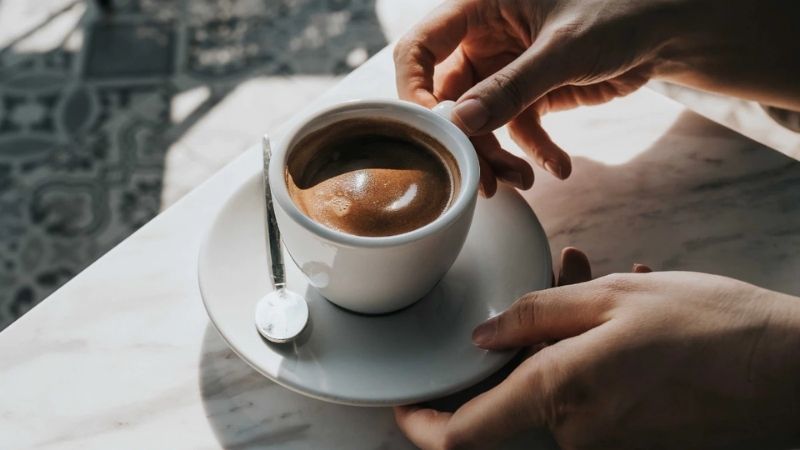 Hai tay nhẹ nhàng nâng tách cà phê espresso nóng hổi