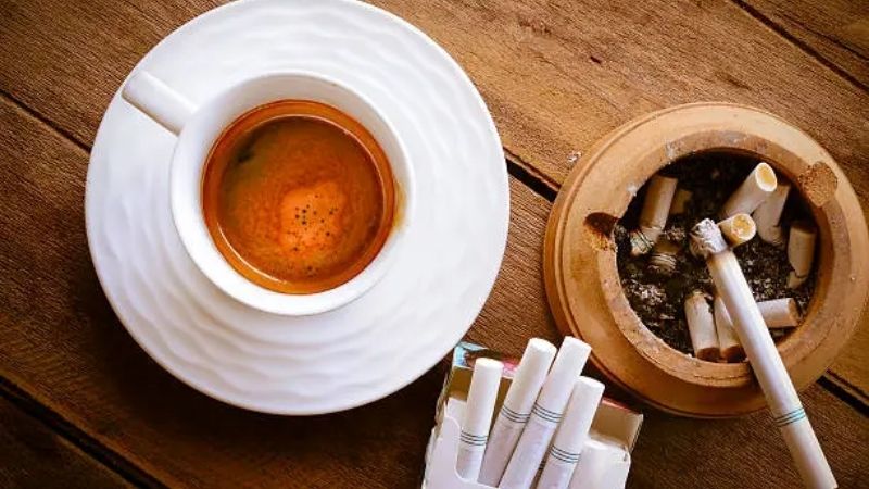 Espresso nóng hổi bên gạt tàn thuốc trên bàn gỗ
