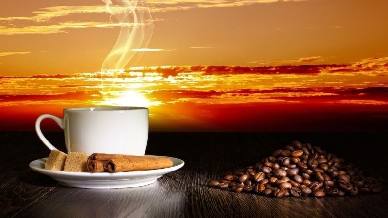 Tách cà phê trắng bên cạnh hạt cà phê dưới ánh hoàng hôn