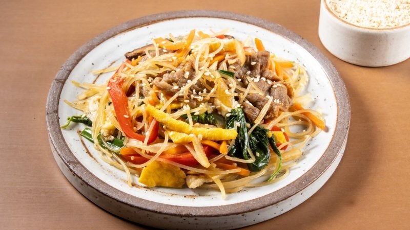 Luộc miến, xào thịt và rau củ, sau đó trộn đều với nước tương, dầu mè và gia vị