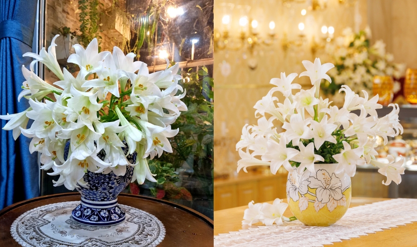 Bình thấp cổ với hoa loa kèn cắm tròn, xen kẽ lá xanh, đặt trên bàn ăn nhỏ